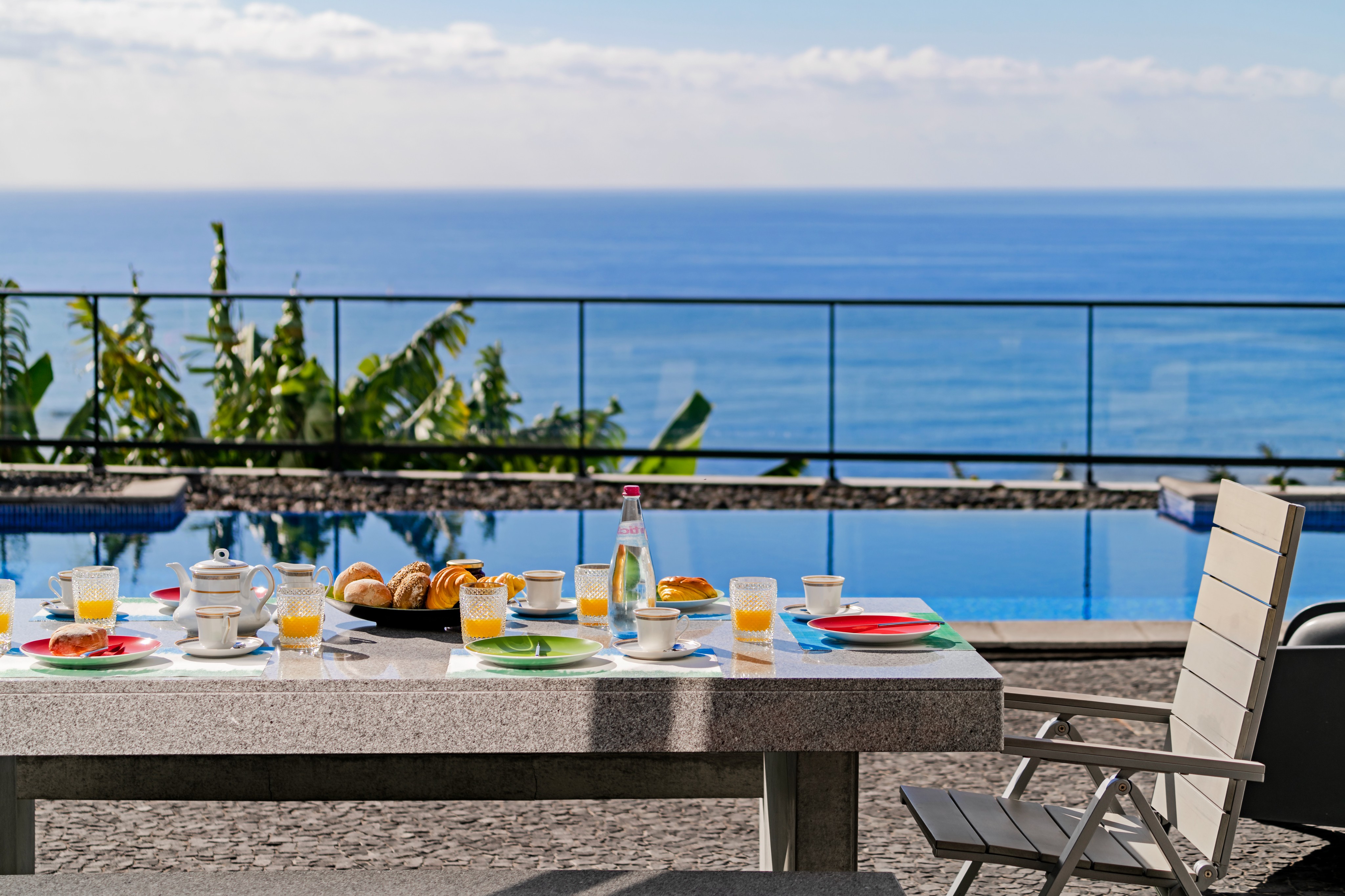 Close Up Of The Outdoor Breakfast Table At Graycis House By Ourmadeira With Fresh Food In Focus And The Swimming Pool And Ocean Softly Blurred In The Background