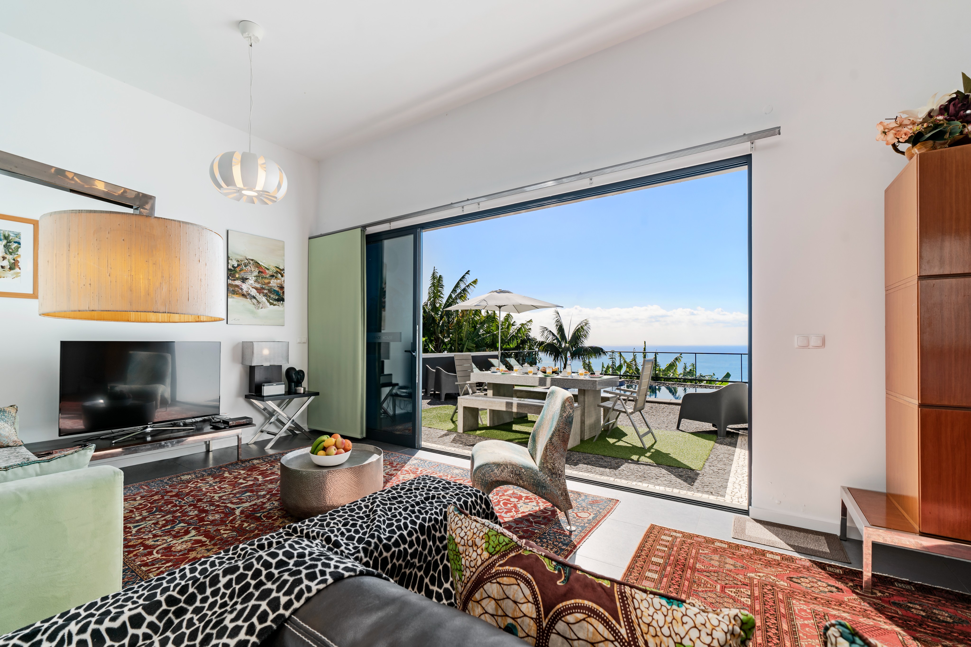 View From The Living Room At Graycis House By Ourmadeira Looking Out Onto A Set Breakfast Table Swimming Pool Lush Surroundings And The Ocean As A Scenic Backdrop