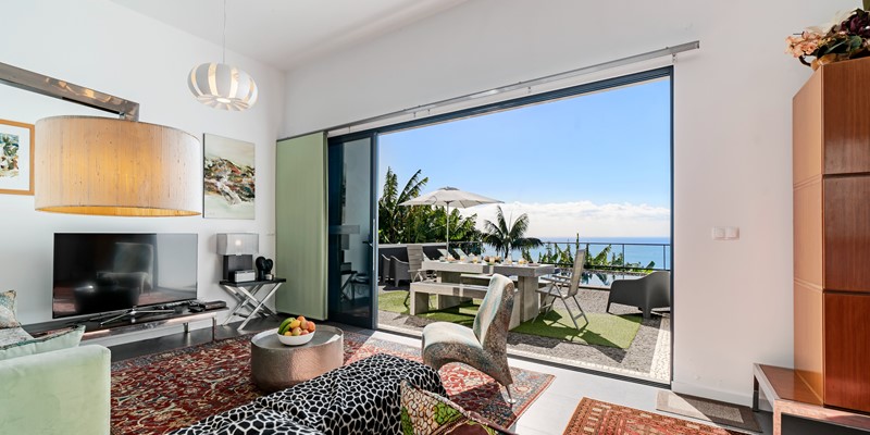 View From The Living Room At Graycis House By Ourmadeira Looking Out Onto A Set Breakfast Table Swimming Pool Lush Surroundings And The Ocean As A Scenic Backdrop