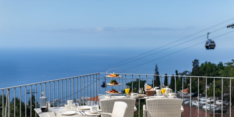 Outdoor Breakfast Setup On The Terrace At Babosas Village By Ourmadeira With Stunning Views Of The Sea And Madeira Cable Car In The Background Offering A Peaceful And Scenic Dining Experience